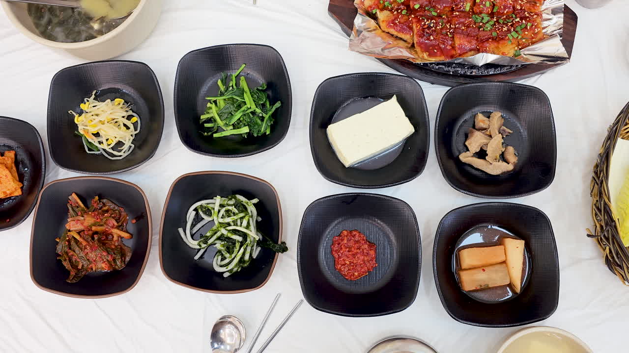 매운 마리네이트 된 생선, 김치와 초록색, 토푸, 해조류 수프를 포함한 다양한 사이드 요리, 모두 색 테이블에 끔하게 제시 된 전통적인 한국 음식의 위에서 아래로 볼 수 있습니다.