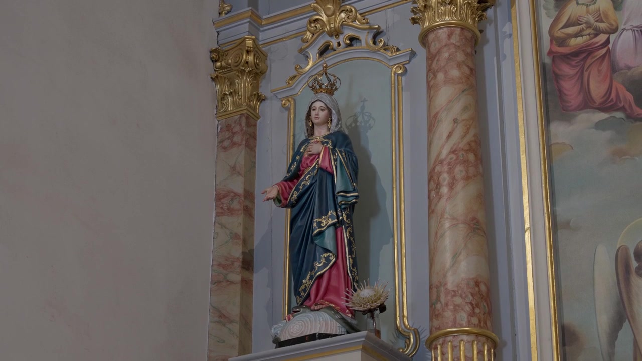 Popis: Malovaná socha Panny Marie s korunou stojí mezi mramorovými zlatými sloupy