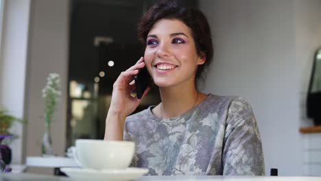 mujer de teléfono inteligente hablando por teléfono mientras estaba sentada en una cafetería con una taza de café en la mesa. ella está sonriendo y riendo en la cafetería