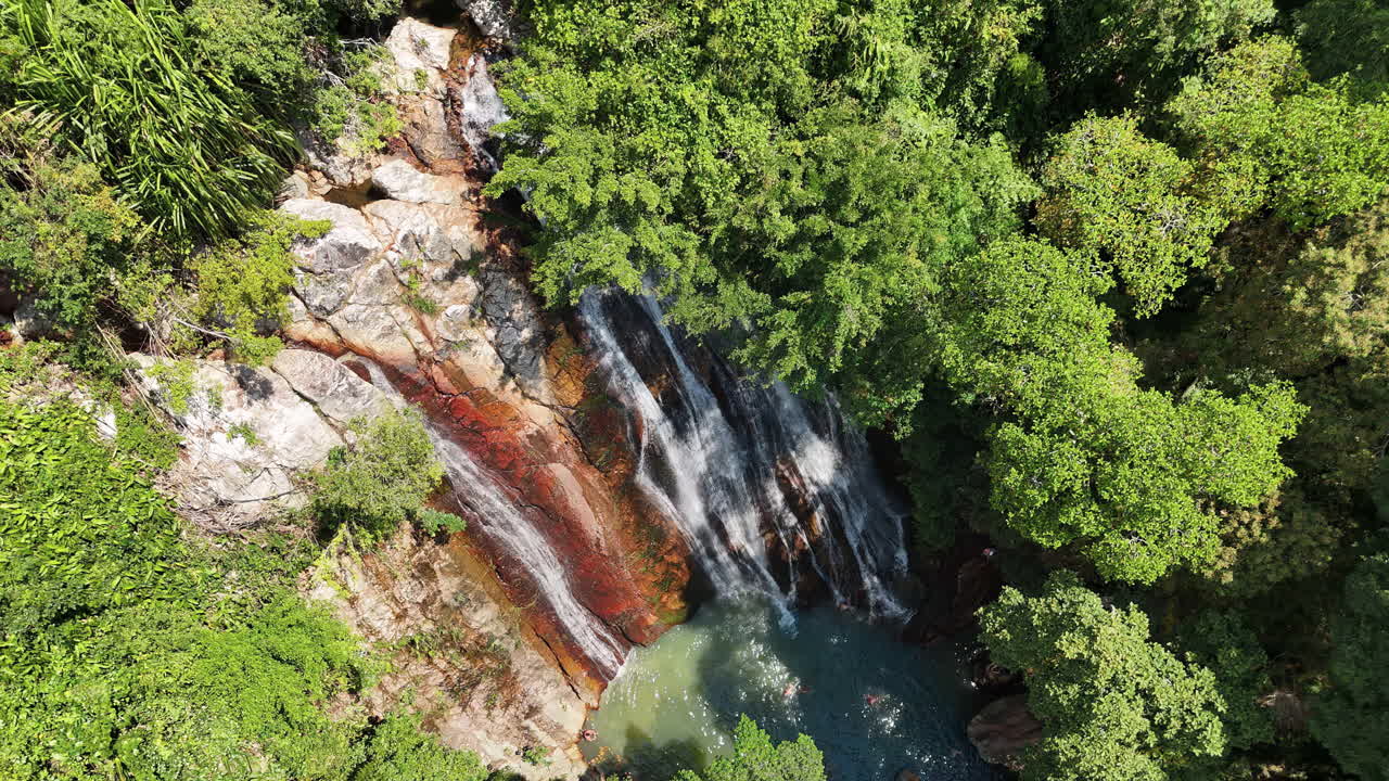 Vista aerea con drone di una cascata tropicale che scorre attraverso una fitta vegetazione della giungla in Thailandia.