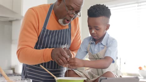 happy african american grandfather and grandson having fun, baking in kitchen, slow motion