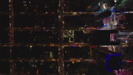 Aerial-birds-eye-overhead-top-down-panning-view-of-stress-and-buildings-in-night-city.-Darker-streets-contrasting-with-area-around-Times--Square.-Manhattan,-New-York-City,-USA