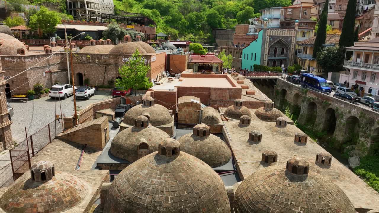 Tiflis'teki Abanotubani kükürt hamamı bölgesinin, ikonik tuğla kubbeleri ve çevredeki renkli evleri gösteren detaylı bir havadan videosu