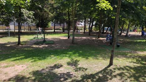 families with children enjoying the games of the public park in the shade of the trees on a sunny summer morning