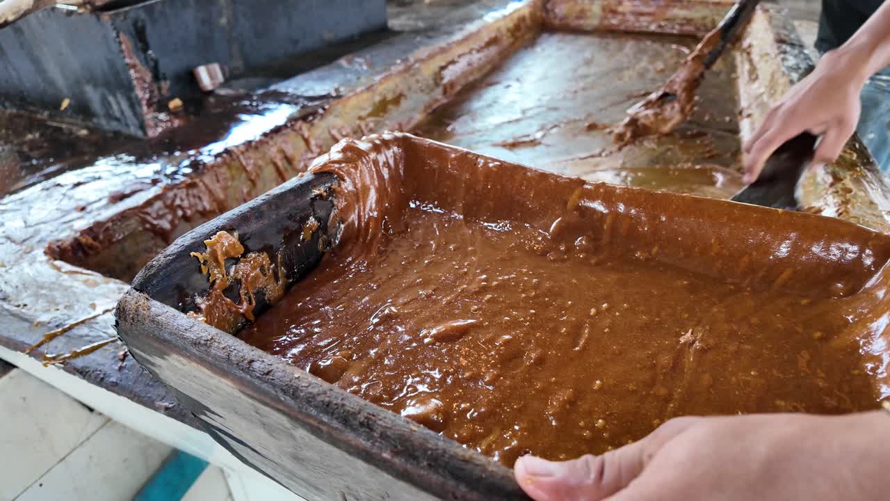 Man stirs thick caramelized sugar in wooden tray with intense, traditional hand motion