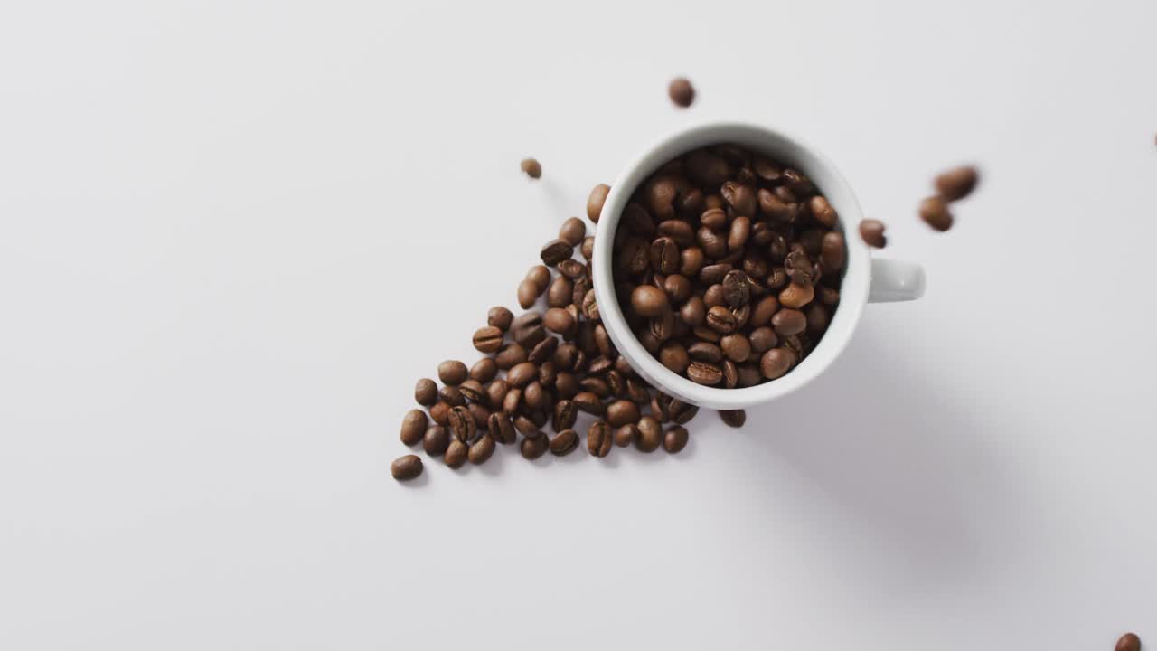 Video af kop kaffebønner over bunke kaffebønner på hvid baggrund