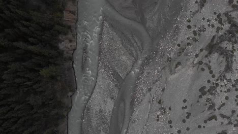 Aerial-bird's-eye-view-over-a-dried-creek-river-with-an-alpine-green-forest-near,-rotate-shot,-conservation-concept