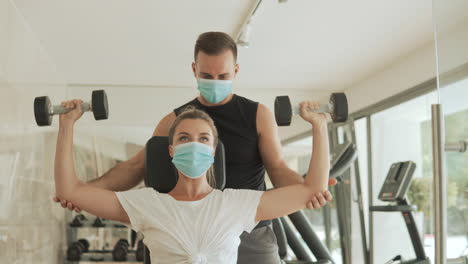 Joven-Atleta-Mujer-Levanta-Pesas-Y-Hombre-Con-Mascarilla-Haciendo-Ejercicio-En-El-Gimnasio