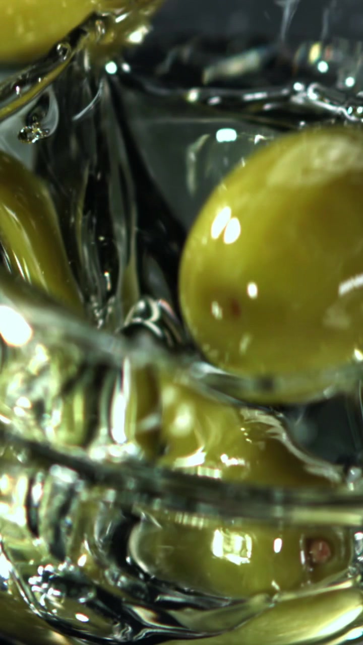 Olive verdi che cadono in un liquido al rallentatore