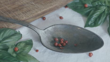 red peppercorns are dropped into a silver spoon and bounce all around on the white tablecloth