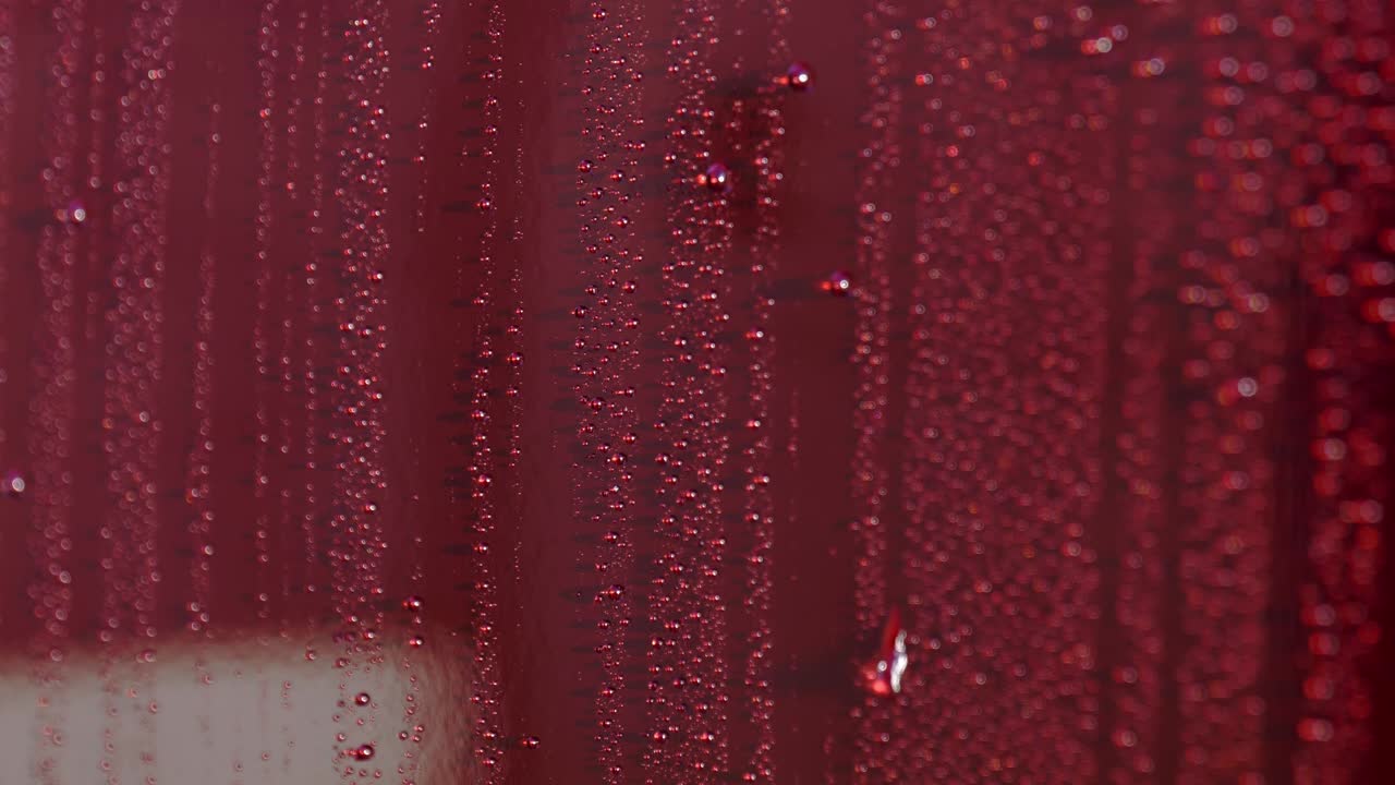 Extreme close up of water beads rolling down dark cherry red car paintwork in the sun