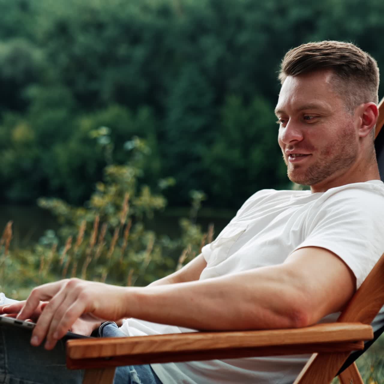 Joyful smiling Caucasian man works on laptop. Freelance businessman working remotely in nature