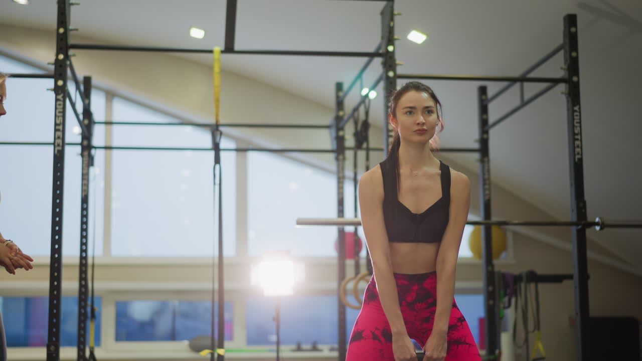 Atleta focado realiza levantamento terra com kettlebell de forma controlada sob a orientação do treinador, com iluminação de estúdio brilhante e cenário de equipamento, respiração constante, instrução de técnica precisa, sorriso sincero e uma atmosfera de treino empoderadora.