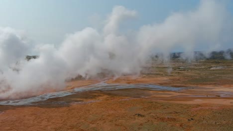 Aerial-Past-Steaming-Hot-Fumeroles-In-A-Geothermal-Aera-Reveals-The-Pretty-Reykjanes-Lighthouse-In-The-Distance