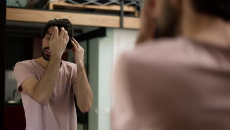 Handsome-young-man-combing-hair-in-mirror,-put-on-headphones-getting-ready-to-go