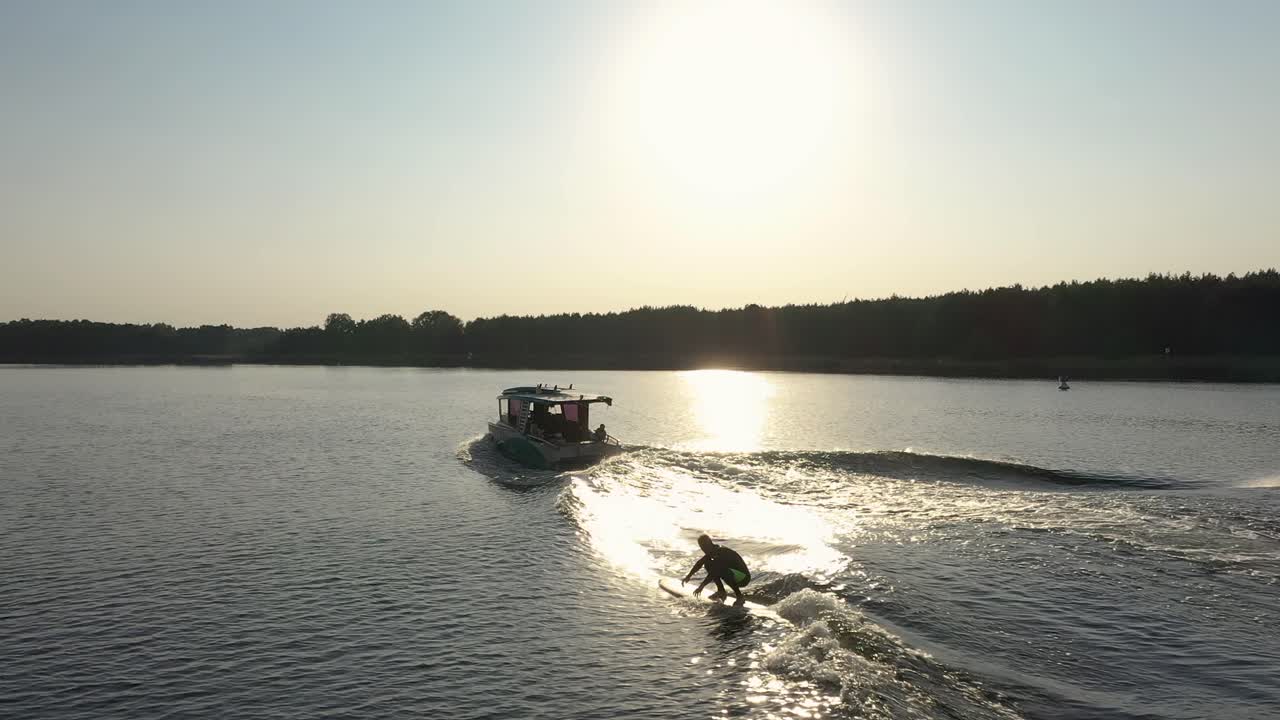 Surfista su tavola da surf che cavalca le onde dietro una barca al tramonto 001.