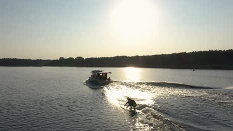 surfer on surfboard surfing waves behind boat in sunset 001