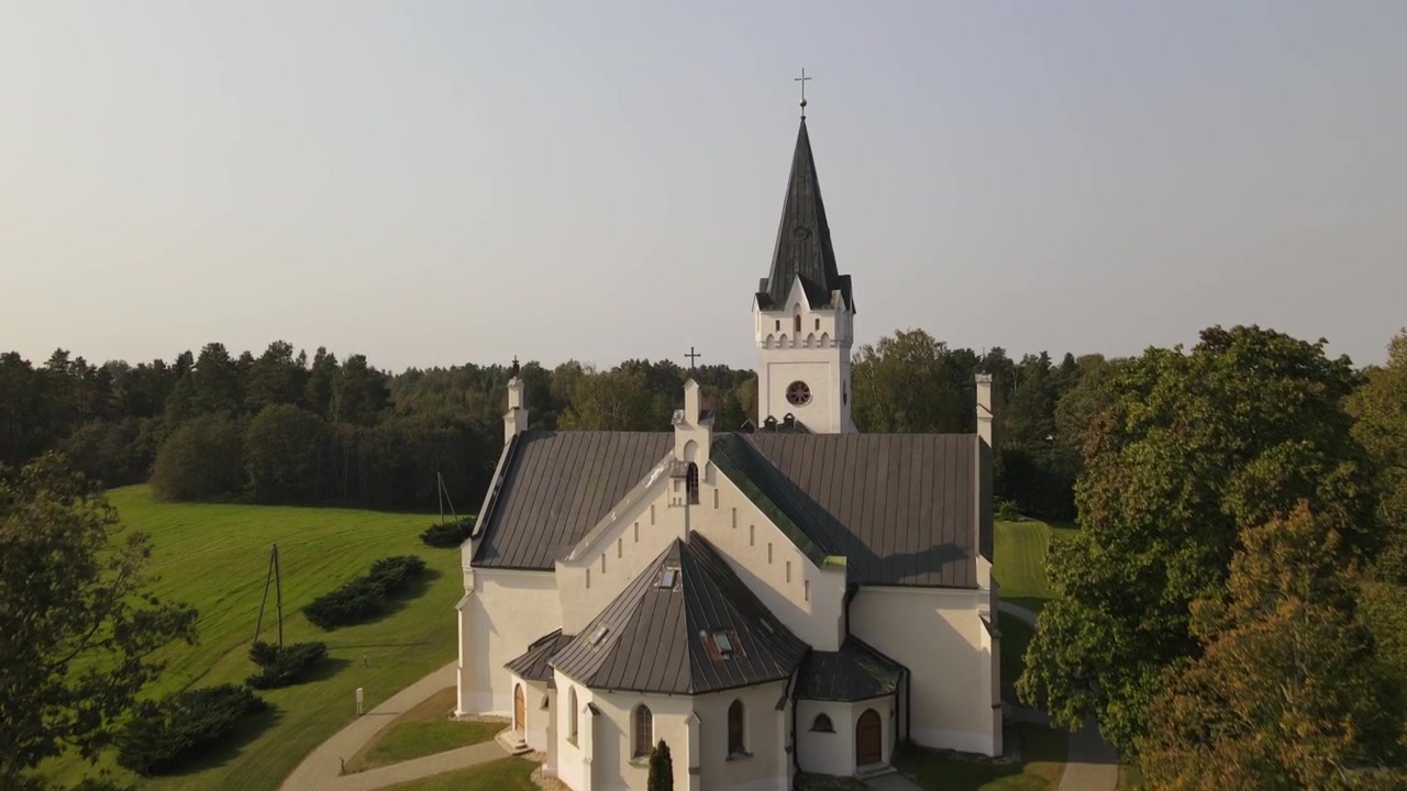 Droneutsikt over St. Thomas evangelisk-lutherske kirke i Jaunpiebalga, fanget på en lys dag. Kirken skiller seg ut blant bygningene i byen, omgitt av grøntområder og gater