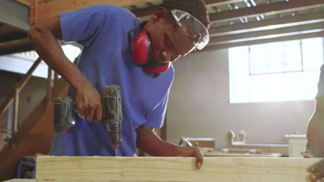 african american coworkers operating drill in shop once coworker joining, stabilizing plank