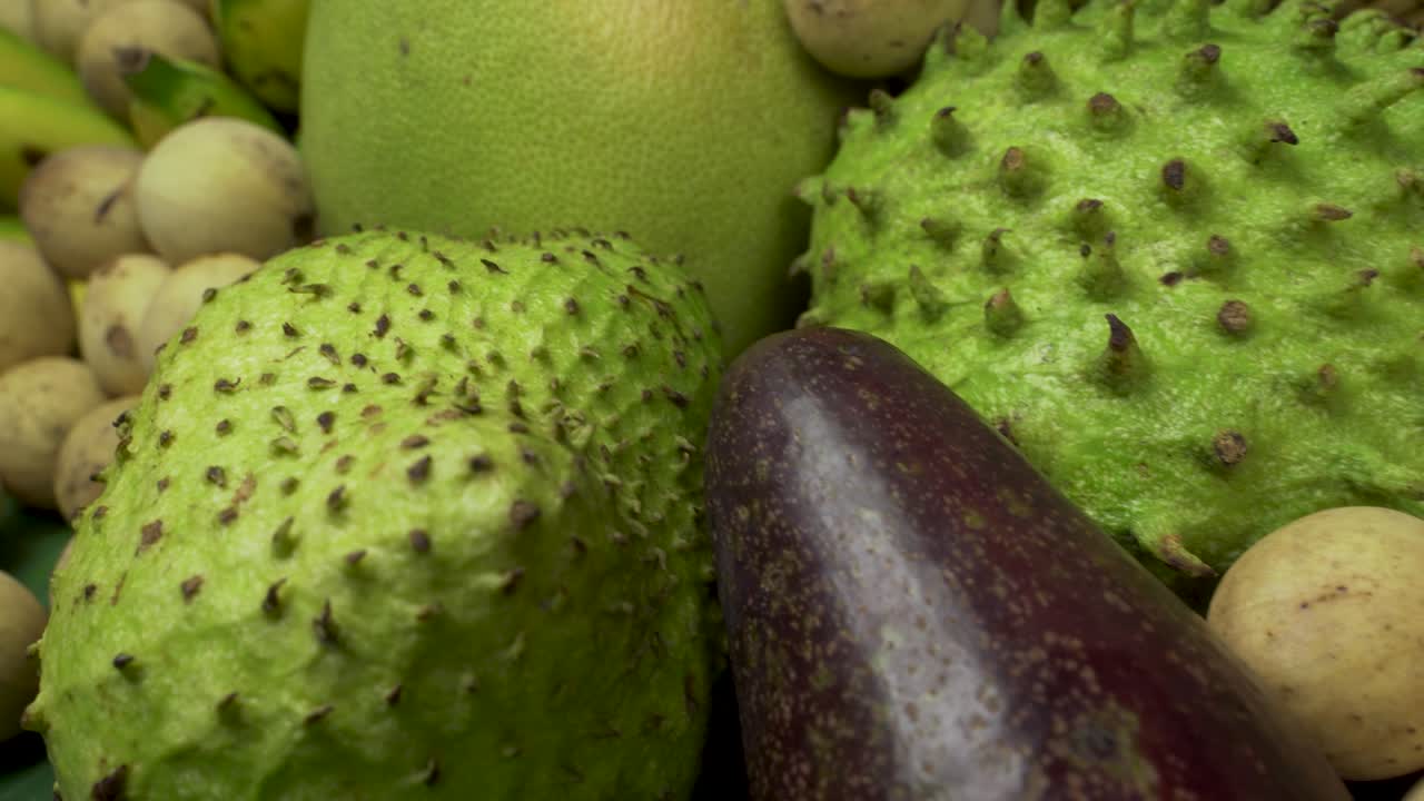 This captivating image showcases an assortment of tropical fruits commonly found in Asia, beautifully arranged with a vibrant hibiscus flower as a centerpiece.