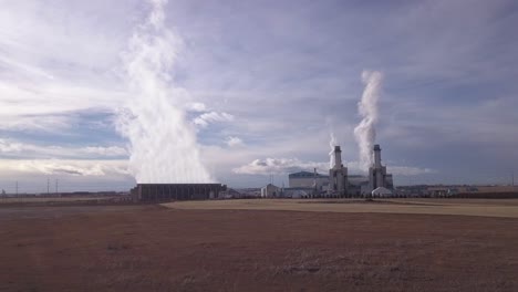 Approaching-low-aerial-of-gas-powered-electrical-plant-belching-steam