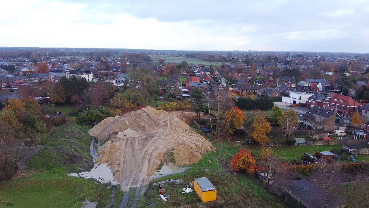 Aerial above residential neighborhood in Belgium and construction site with hill of sand during rainy day.