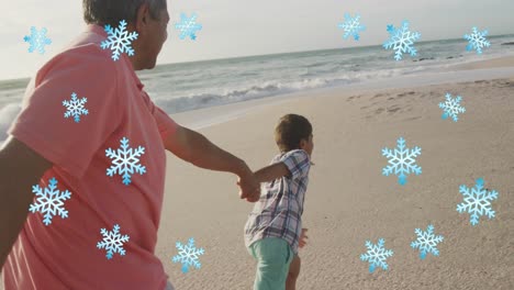 Animation-of-snowflakes-over-happy-hispanic-grandfather-and-grandson-having-fun-on-beach