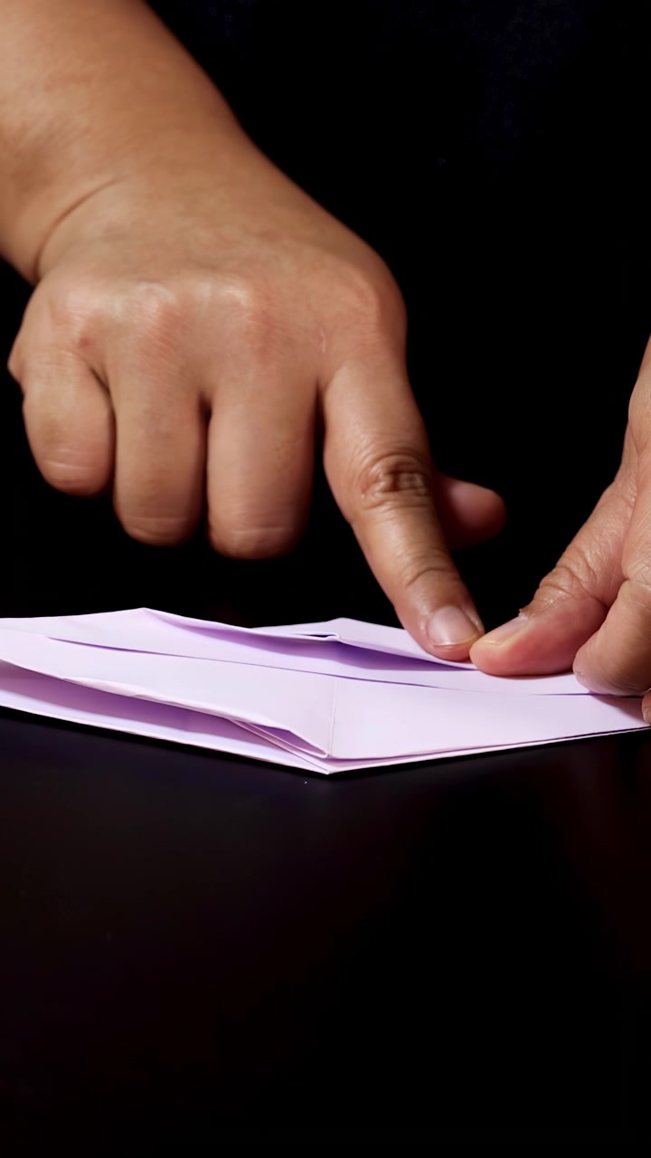 Mani adulte piegano con cura carta leggera su una superficie nera sotto un'illuminazione da studio morbida e controllata