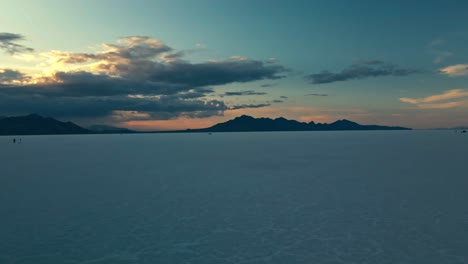 Vorwärtsantenne-Auf-Utah-Salt-Flats-Mit-Reifenspuren-Und-Spärlichen-Wolken-Und-Der-Sonne-Am-Horizont