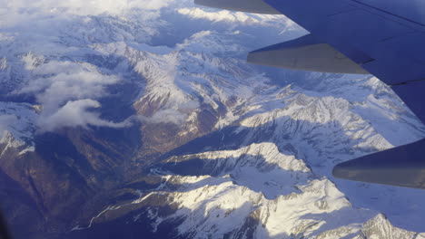 dramatic view out of plane window of swiss alps and mountains covered in snow with blue sky and fluffy white clouds