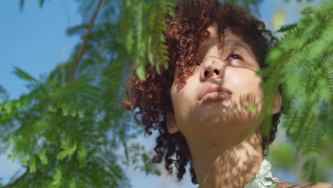 Low-angle-facial-close-up-of-a-brown-eyed-girl-in-a-park-with-leaves-in-the-foreground