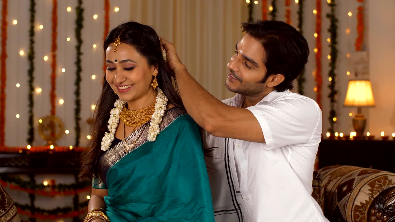 un marido del sur de la india ayudando a su hermosa esposa a prepararse para el festival poniendo gjara - pasando tiempo juntos en diwali