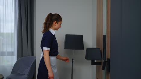 a maid in a hotel room turning on a floor lamp