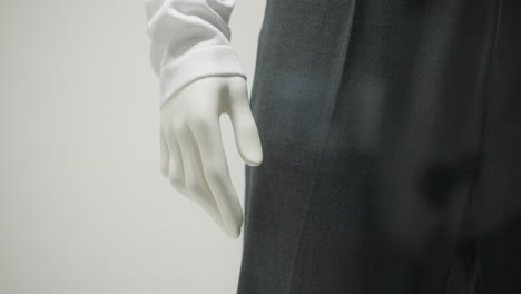 partial view of mannequin hand wearing long white sleeve and black trousers, showcasing elegant clothing detail with soft lighting, minimalist composition, and clean background