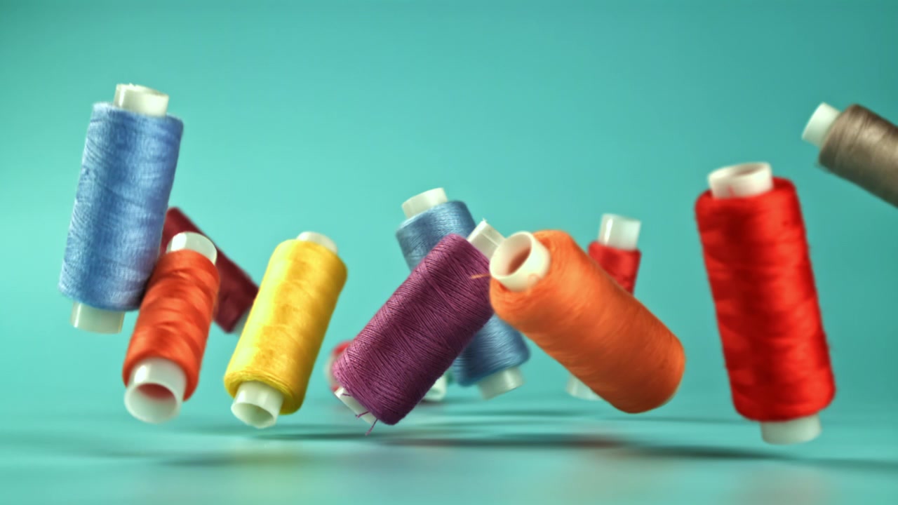 Colorful Thread Spools Falling in Slow Motion on Teal Background