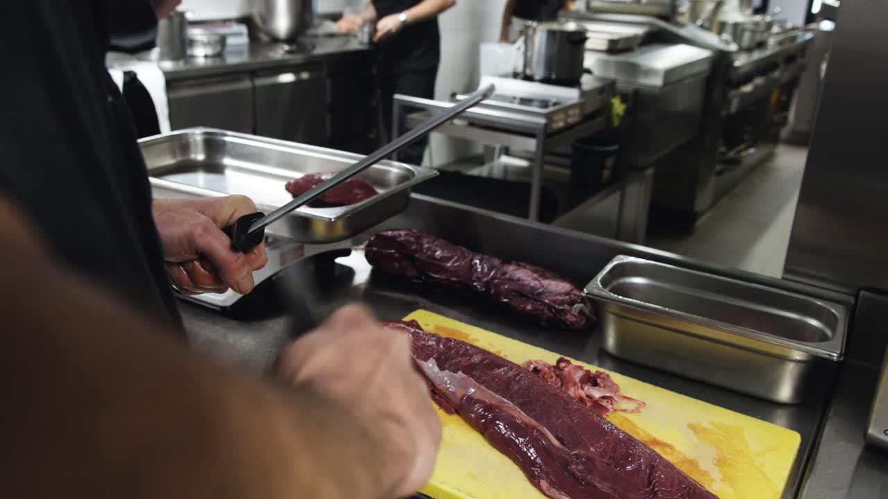 slow motion handheld shot di chef che affila un coltello per tagliare la carne in una cucina di fascia alta