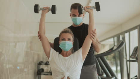 athlete woman lifts weights and man with face mask exercising in the gym