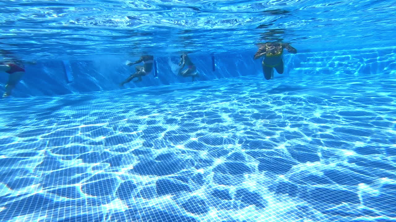 People swimming in the swimming pool. Underwater video of children's legs and woman's body swimming in transparent blue water.
