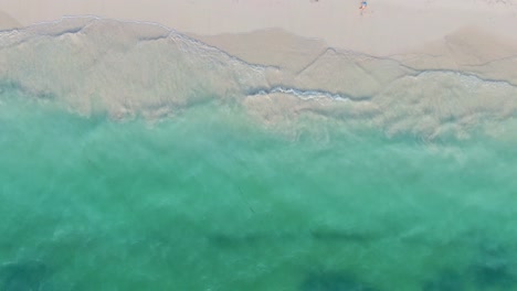 Tropical-beach,-waves-washing-ashore,-turquoise-sea,-aerial-top-down-drone-view-of-white-sand-beach-and-unrecognizable-woman-walking