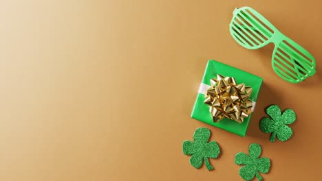 Video-of-saint-patricks-day-green-shamrock,-present-and-glasses-with-copy-space-on-orange-background