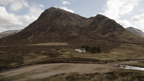 aerial of lagangarbh hut white cottage in glencoe scottish highlands with mountain buachaille etive mor in the distance