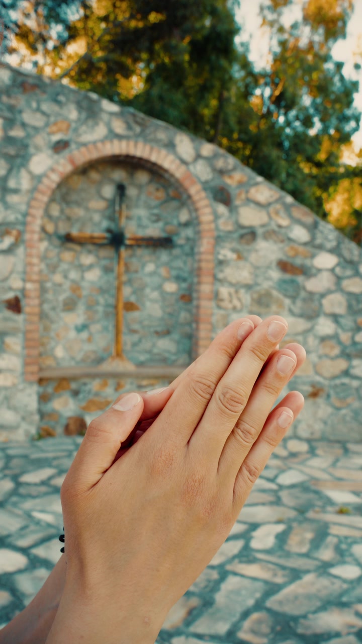 Mani giunte in preghiera di una donna cristiana davanti a un crocifisso all'aperto