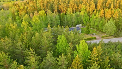 aerial: rural house with pv panel roof in middle of vibrant woods, summer sunset