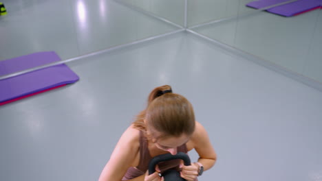 top-down view of fit woman lifting weight during intense workout in modern gym, large mirror in background reflecting gym environment, fitness mats, and training equipment