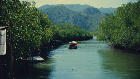 a long-tailed boat sails out into a river in a thai national park