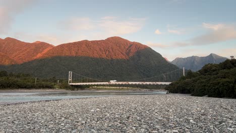 campista cruzando un viejo puente de acero oxidado en el remoto desierto de la costa oeste de nueva zelanda al atardecer