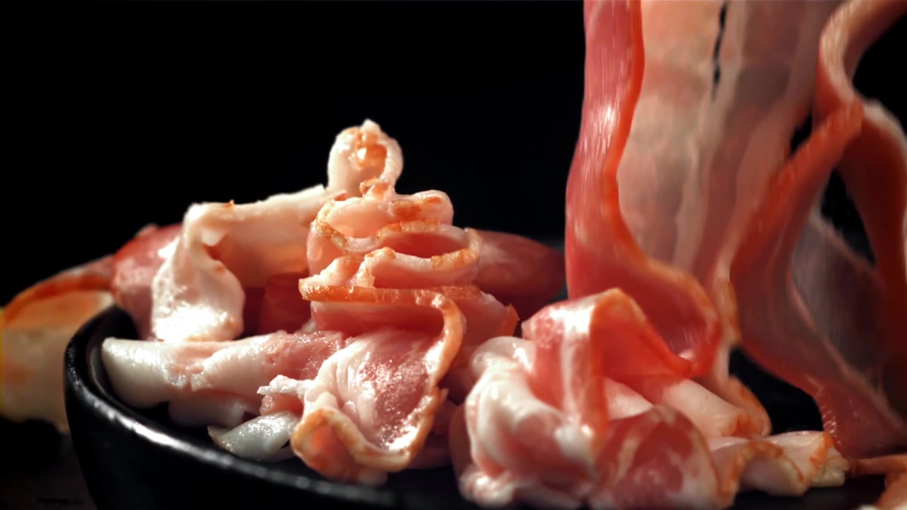 Fette di pancetta cruda che cadono al rallentatore su un piatto nero