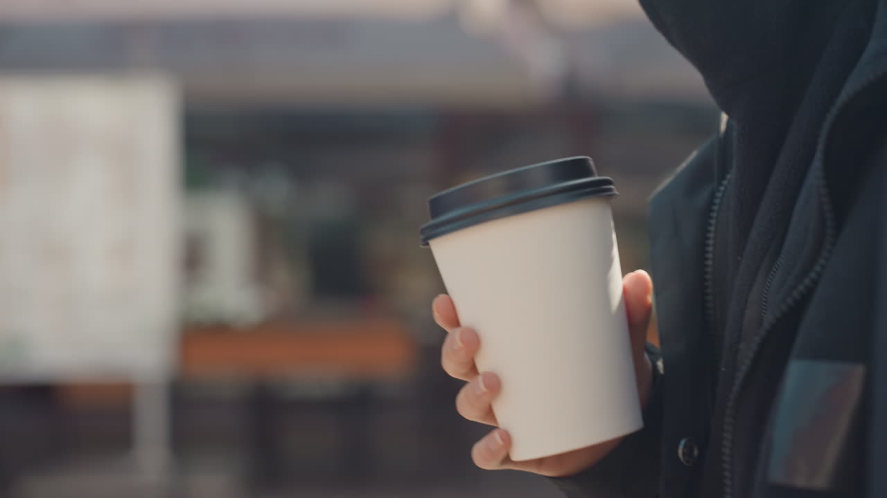 Primo piano di una tazza di caffè, vista dettagliata di una tazza di caffè su uno sfondo di mercato vivace con tonalità calde, scatto mirato di una mano che stringe una tazza di caffè in un contesto vivace di strada cittadina con toni tenui