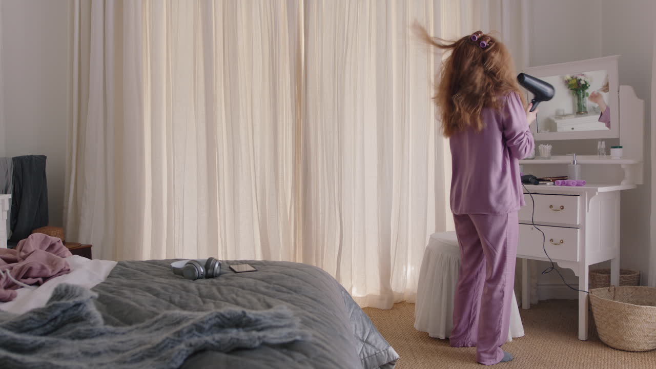 mujer divertida bailando en el dormitorio cantando karaoke con secador de pelo disfrutando de la mañana del fin de semana divirtiéndose celebrando un estilo de vida despreocupado usando pijama en casa