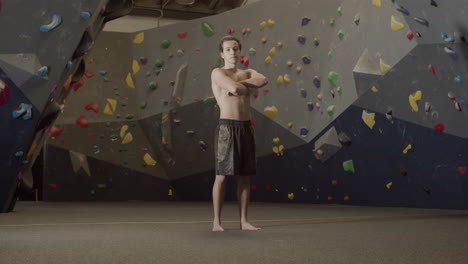 retrato de un joven deportista sin camisa parado en un gimnasio de boulder y mirando la cámara